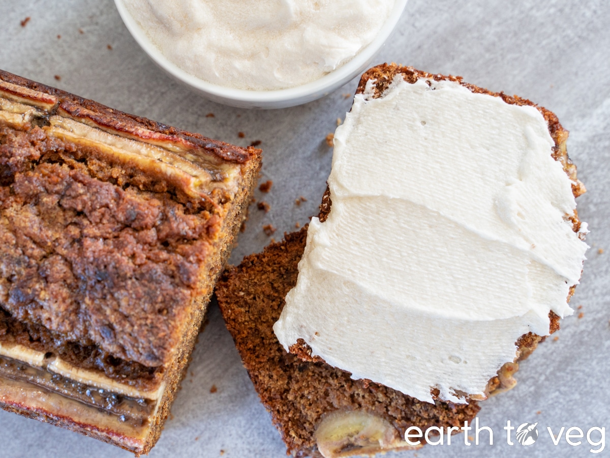 top down view of a loaf of rye banana bread with two thick slices covered in vegan cream cheese