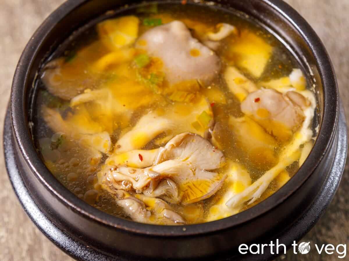 Oyster mushroom soup with ginseng, scallions, and golden broth in a clay pot.